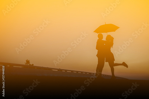 Silhouettes of couple against umbrella the sunset.