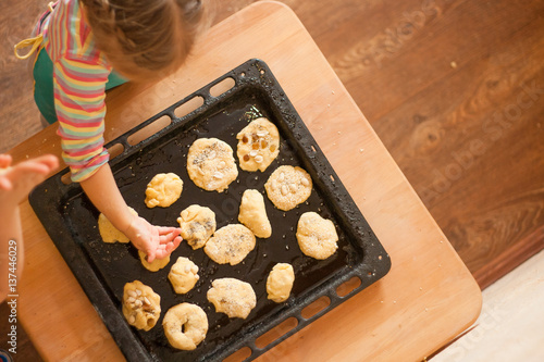 Little girl puts hand made biscuits on baking tray in Waldorf kindergarten