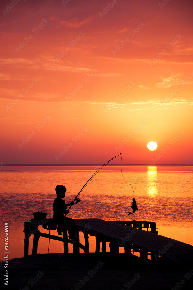 Boy fishing in ocean surf at sunset.