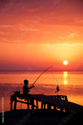 Boy fishing in ocean surf at sunset. © Anatoliy