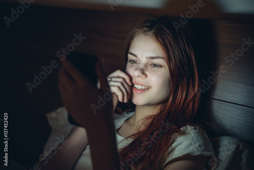 happy woman in bed looking into phone