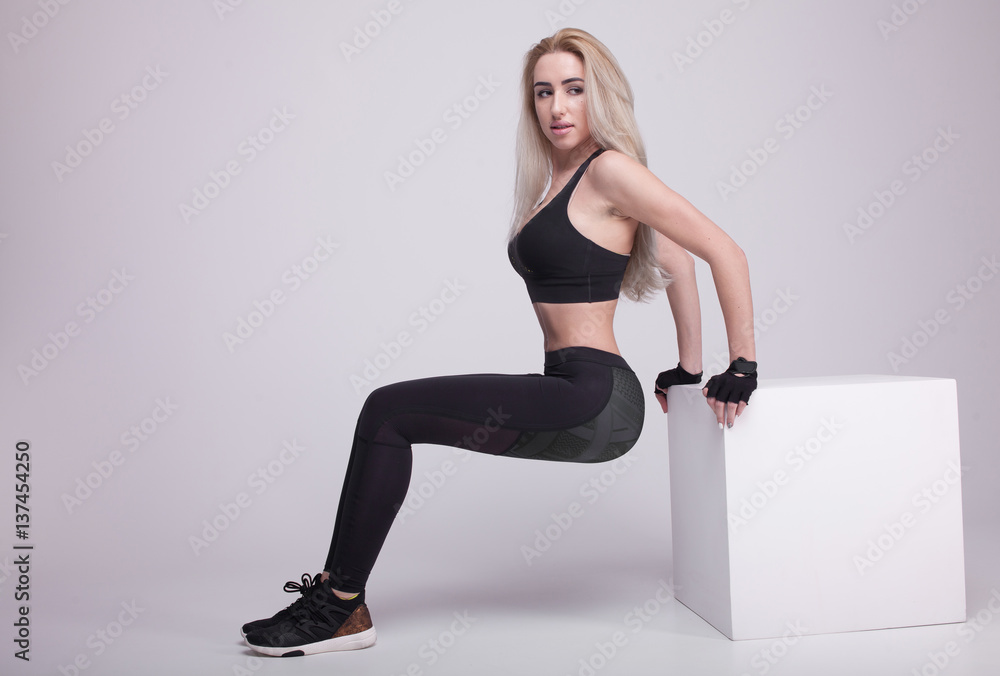 Young positive fitness blonde woman training with white cube. Slim woman in sport clothes.