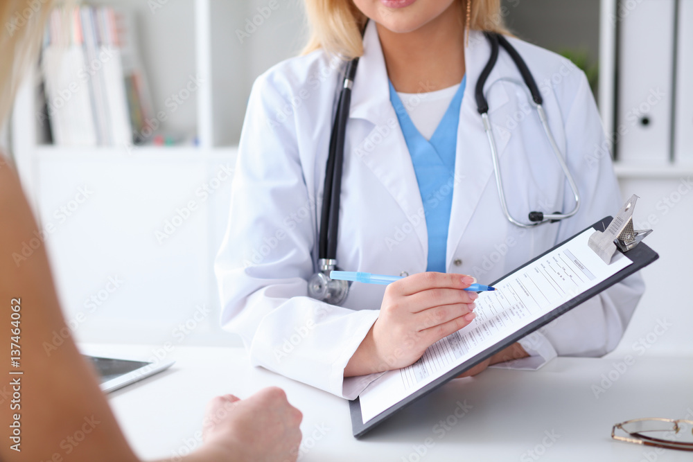 Close up of a doctor and patient hands while phisician pointing into medical history form at clipboard. Medicine and health care concept Close up of a doctor and patient hands while phisician pointing into medical history form at clipboard. Medicine and health care concept