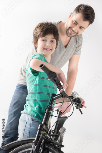 smiling father and son holding bicycle on white