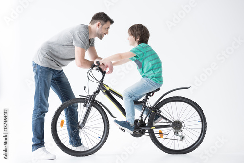 side view of father talking with son on bicycle on white