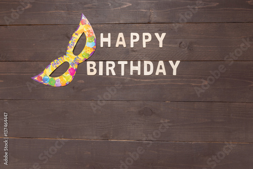 Happy Birthday and mask are on wooden background