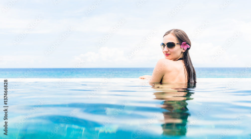 Woman with red bikini and flower in hair in infinity Pool