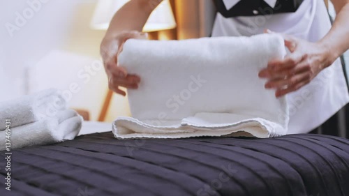 Middle-aged Caucasian female chambermaid folding towels on bed in slowmotion photo