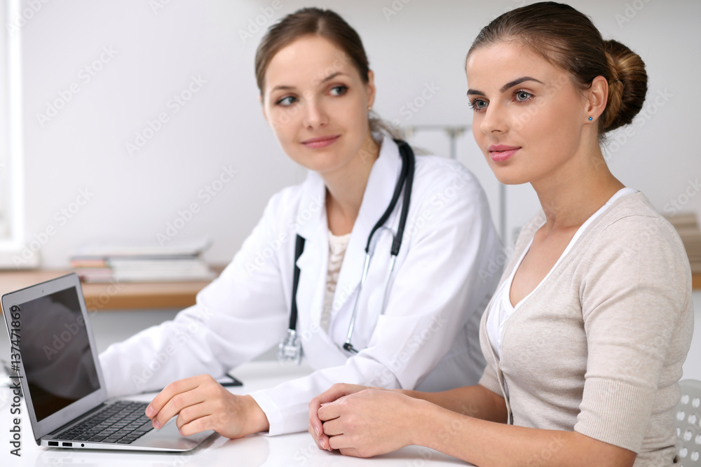 Doctor and patient sitting at the desk. Physician pointing into laptop computer. Medicine and health care concept Doctor and patient sitting at the desk. Physician pointing into laptop computer. Medicine and health care concept