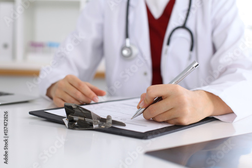 Close up of a female doctor filling up an application form while consulting patient. Medicine and health care concept