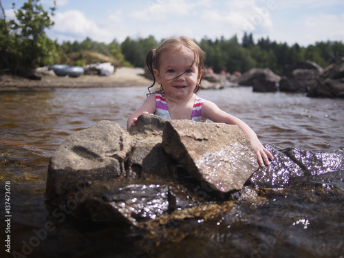 A toddler holds on to a rock while wading in Flagstaff Lake; Maine, United States of America photo