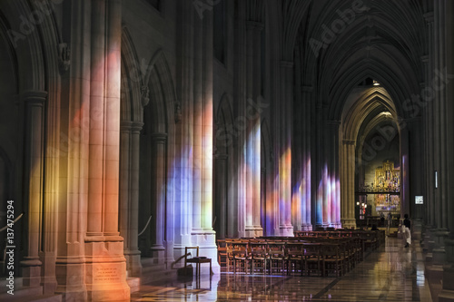 Light streaming through stained glass windows with colourful light columns along the cathedral nave, altarpiece in St. Mary's Chapel visible background; Washington, District of Columbia, United States of America photo