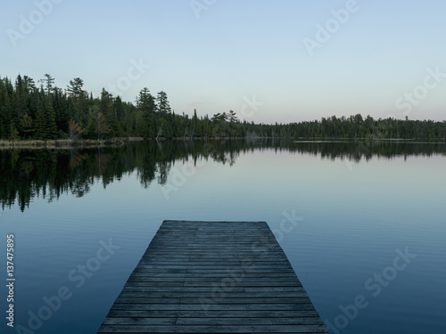 Wooden dock leading out to a tranquil lake at sunrise; Whiteshell, Manitoba, Canada photo
