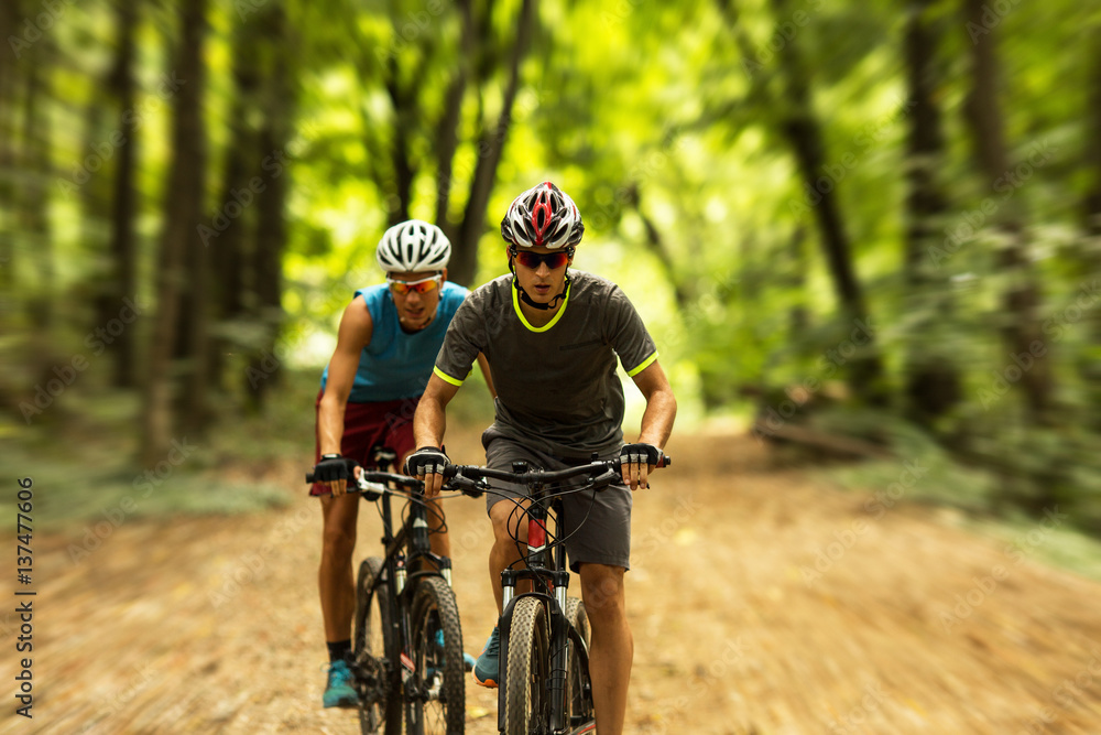 Two mountain bikers riding bike in the forest on dirt road. Two mountain bikers riding bike in the forest on dirt road.
