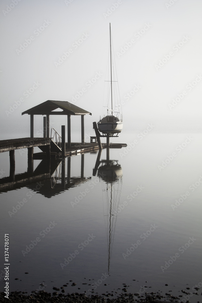 Sailboat on lift by dock on foggy lake; Bellingham, Washington, United States of America Sailboat on lift by dock on foggy lake; Bellingham, Washington, United States of America