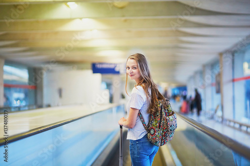 Tourist girl with backpack and carry on luggage in international airport, on travelator