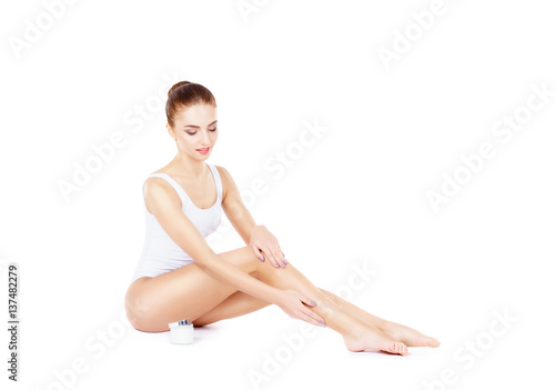 Fit and sporty girl in bodysuit isolated on white. Beautiful and healthy woman adding a cream on her legs. Sport, fitness, diet, weight loss and healthcare concept.