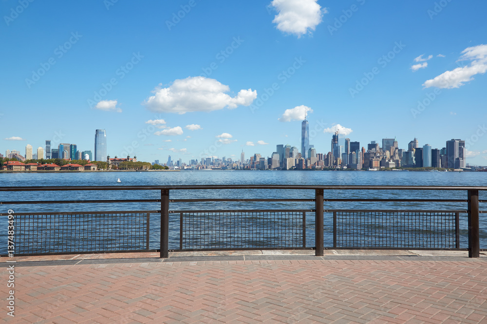 New York city skyline and Ellis Island view from empty dock terrace in a sunny day