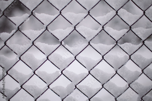 Fence background. Metallic net with snow. Metal fence in winter covered with snow. Wire fence closeup. Texture and background for designers. Wire fence covered by ice and snow. 