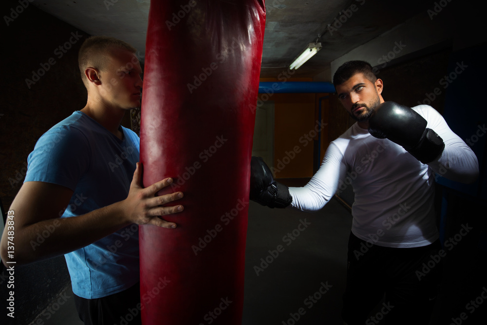 Two young men at the gym are practicing kickboxing punches on punching bag