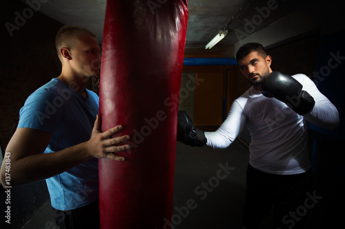 Two young men at the gym are practicing kickboxing punches on punching bag © bokan