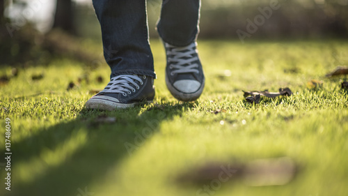 Walking feet ; Man wear blue jean and canvas sneaker sunrise walking on sunrise lawn and landscape background.