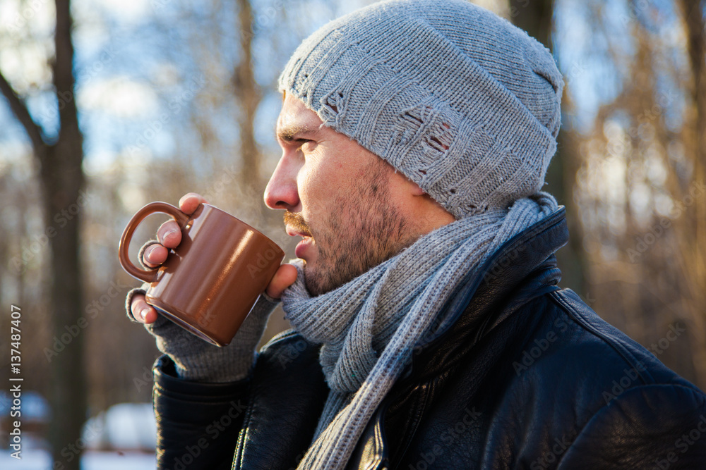 Handsome young man is traveling. He is looking forward in the forest at the nature. Blured background. He is drinking hot tea. Handsome young man is traveling. He is looking forward in the forest at the nature. Blured background. He is drinking hot tea.