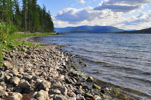 Bank of the lakes on the Putorana plateau. Summer water landscape with stones on the shore in the foreground.