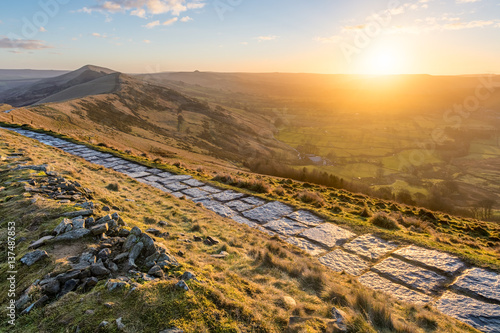 Stone walking path running along ridge of Mam Tor in the British Peak District with sun rising above horizon. photo