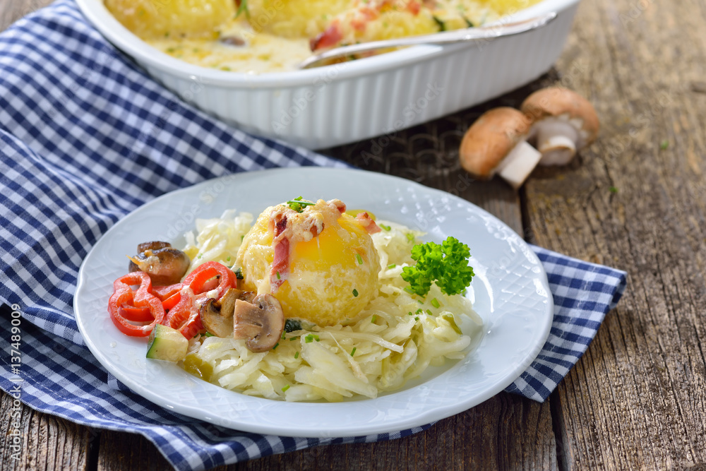 Gratinierter Kartoffelknödel mit Speck und Champignons auf warmem Krautsalat serviert - Hearty potato dumpling gratin with cheese and bacon served on warm cabbage salad Gratinierter Kartoffelknödel mit Speck und Champignons auf warmem Krautsalat serviert - Hearty potato dumpling gratin with cheese and bacon served on warm cabbage salad