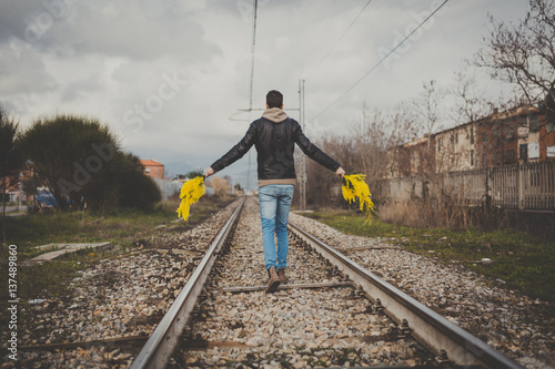 Foto Ragazzo cammina sulla ferrovia con le braccia aperte e delle mimose in mano