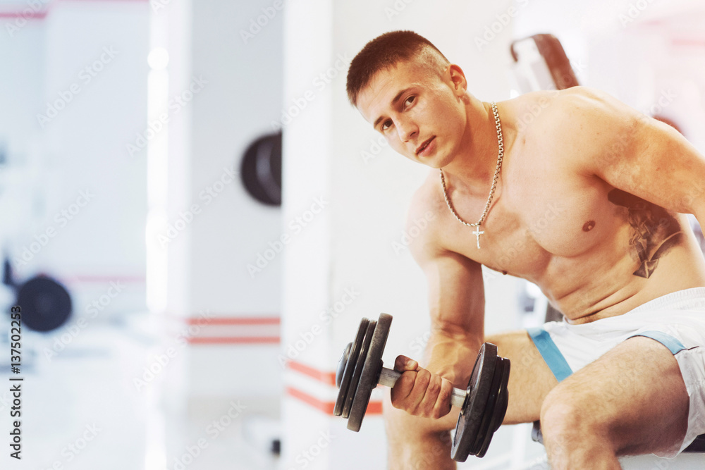 Beautiful athletic bodybuilder guy, carries out exercises with d Beautiful athletic bodybuilder guy, carries out exercises with d