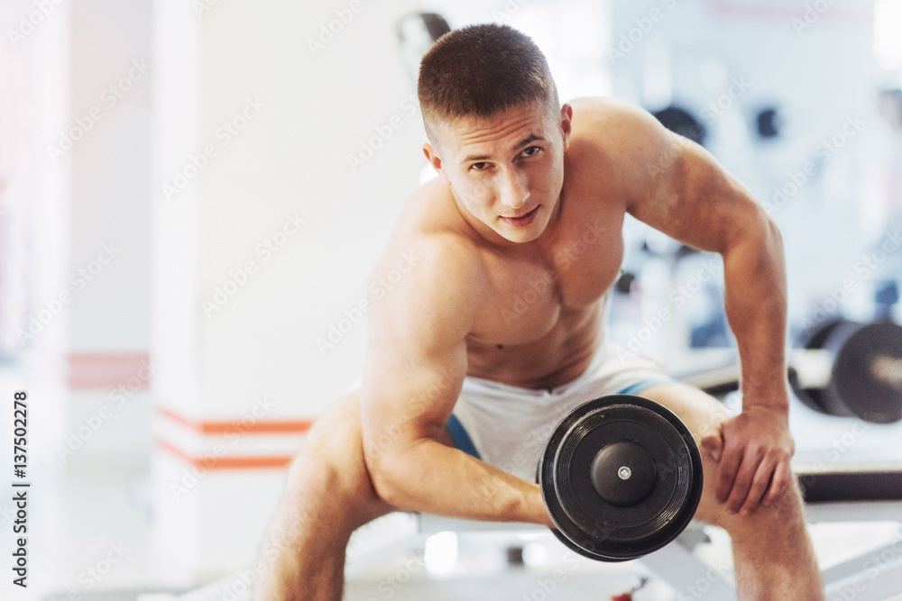 Beautiful athletic bodybuilder guy, carries out exercises with d Beautiful athletic bodybuilder guy, carries out exercises with d