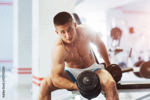 Beautiful athletic bodybuilder guy, carries out exercises with d