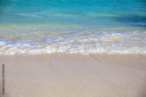 Close up blue sea water waves with bubbles on sand beach