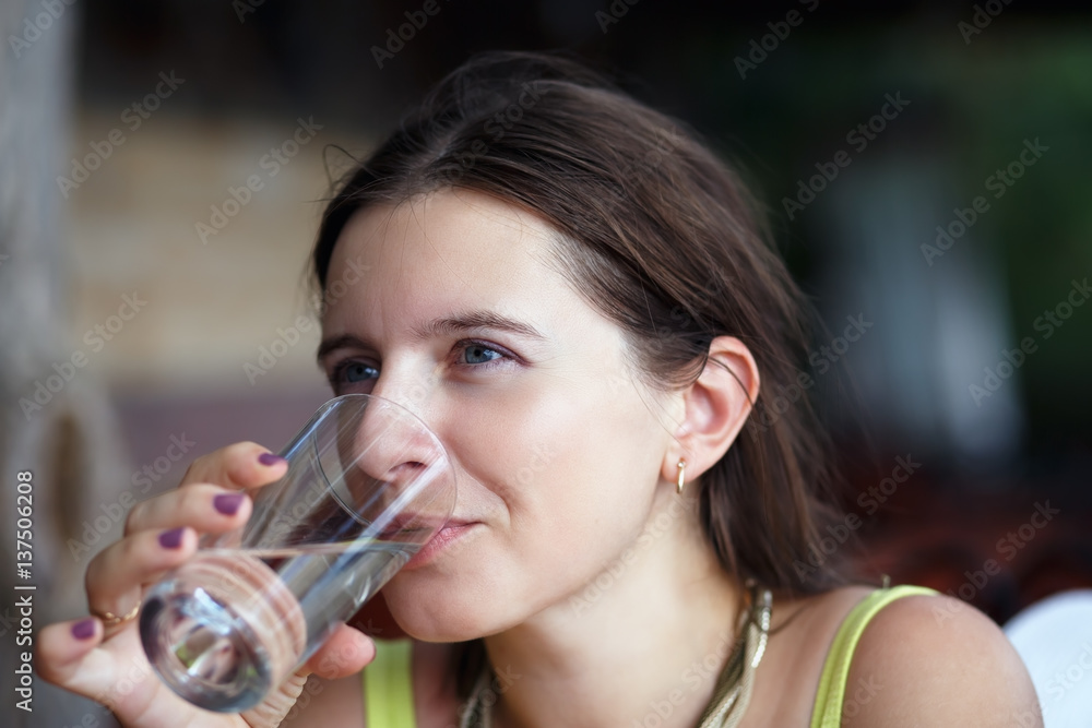Pretty young woman drinking pure water from a transparent glass beaker. Selective focus.