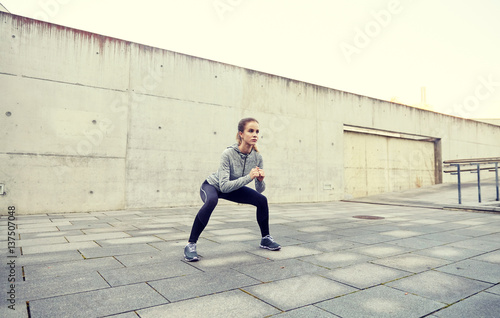 happy woman doing squats and exercising outdoors