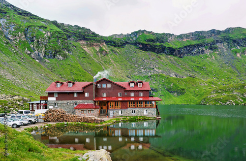Bild auf Leinwand Photo of balea lake in fagaras green mountains at sunset, red house with fog near a lake with reflection, Romania