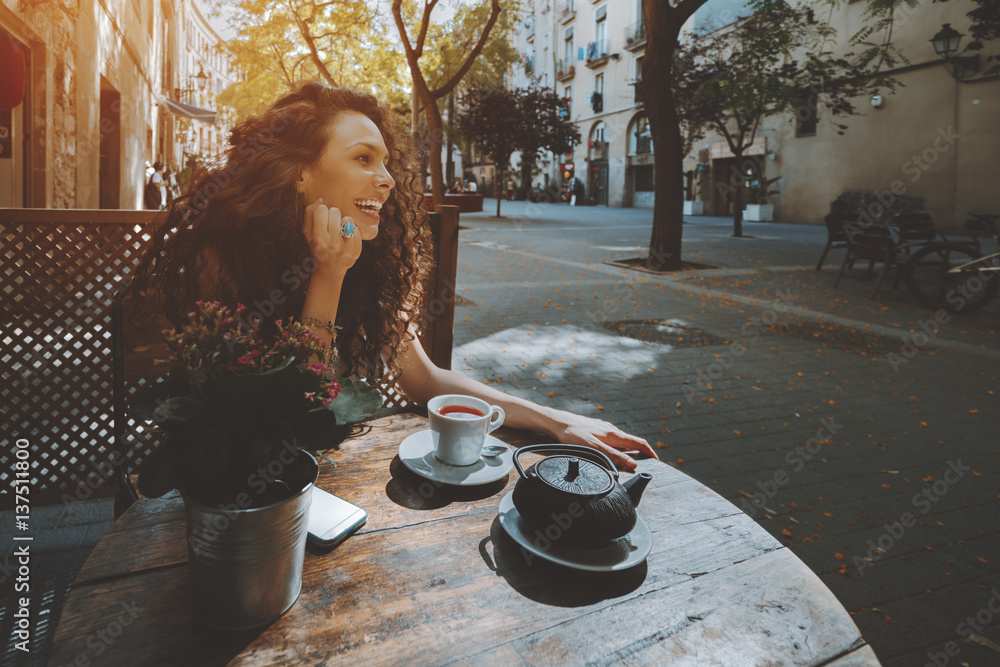 Laughing curly woman with black hair looking away while sitting in cafe during coffee break, smiling Laughing curly woman with black hair looking away while sitting in cafe during coffee break, smiling