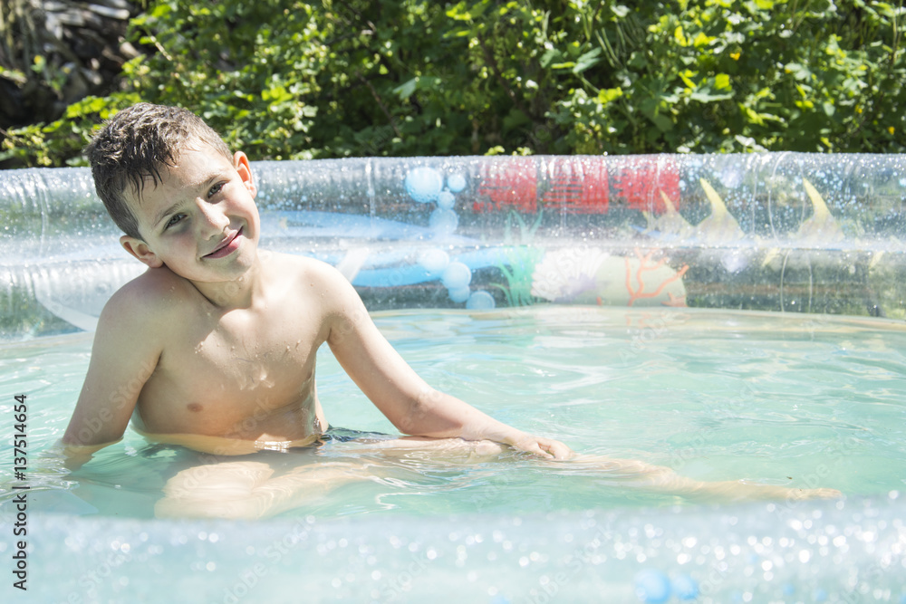 In the summer in the garden boy bathes in inflatable pool.