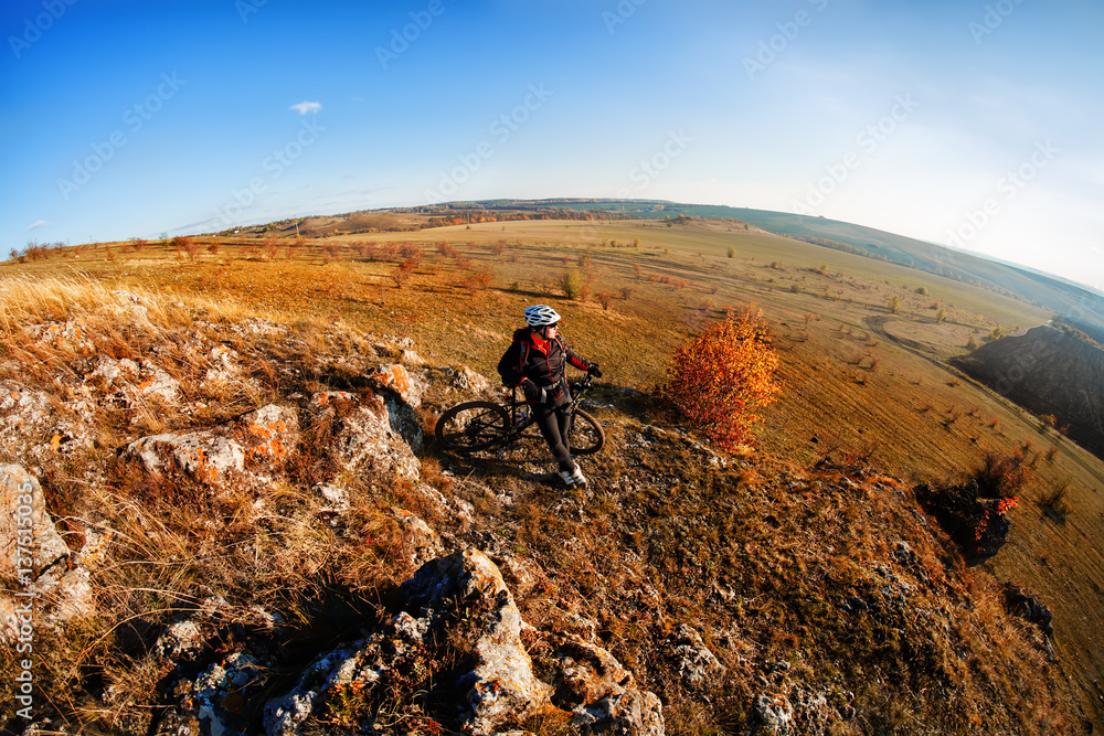 Wide angle view of cyclist standing with mountain bike on trail at sunset.