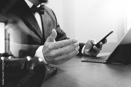 Justice and Law context.Male lawyer hand working with smart phone digital tablet computer docking keyboard with gavel and document on wood table black and white