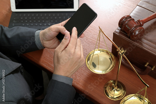 justice and law concept.Male lawyer in office with the gavel,working with smart phone,digital tablet computer docking keyboard,brass scale,on wood table