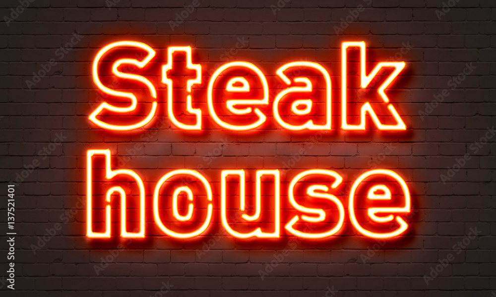 Steak house neon sign on brick wall background.