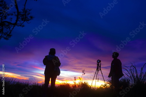Fototapeta Naklejka Na Ścianę i Meble -  hiker with camera making photo on a hill at sunset and clouded sky