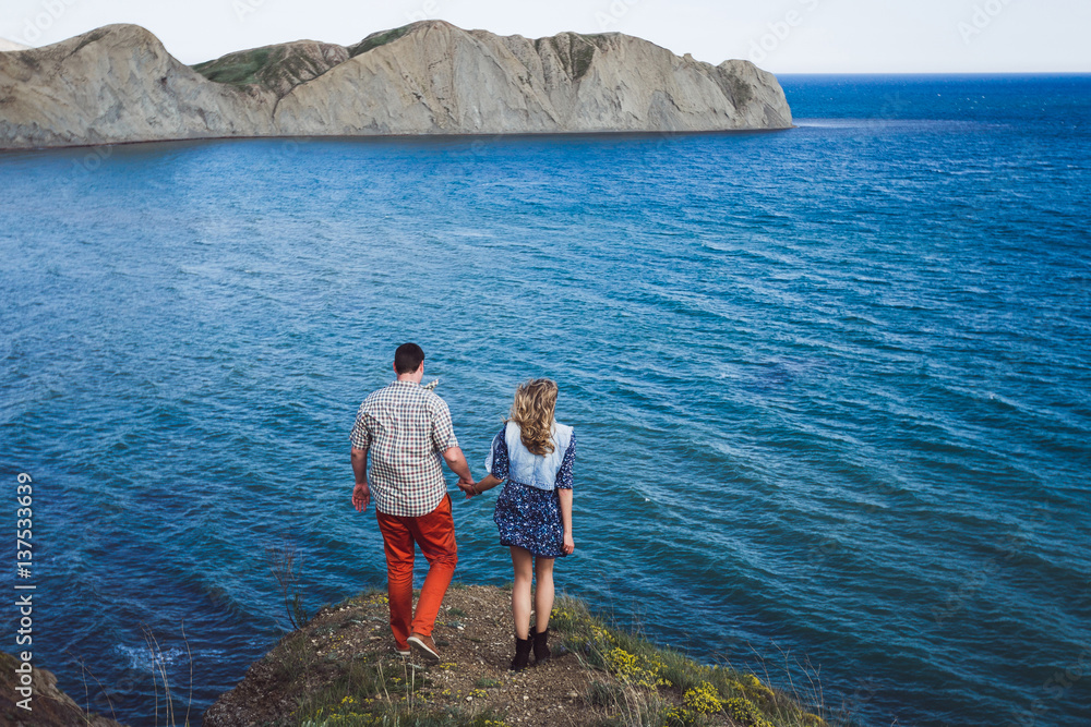 Couple relaxing by the sea with amazing mountain view. Jeans jacket, blue dress, casual style
