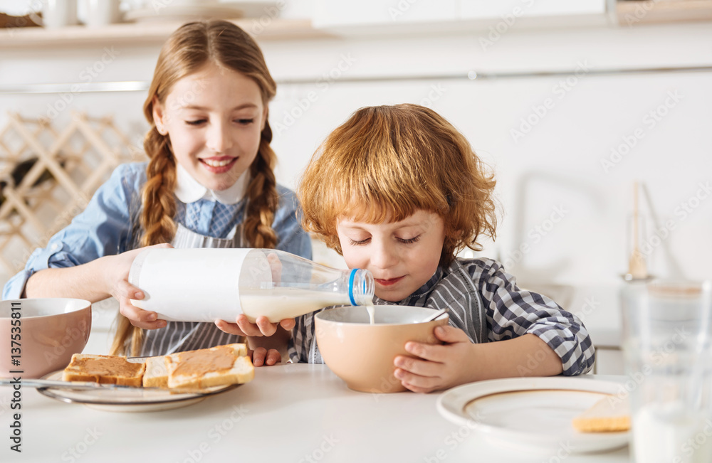 Smiling charming girl pouring milk in a bowl Smiling charming girl pouring milk in a bowl