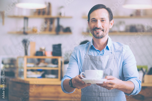 Positive senior waiter holding cup of coffee photo