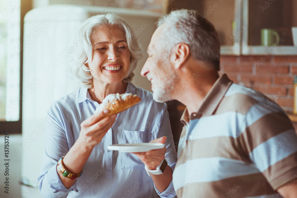 Cheerful aged woman giving croissant to her husband Cheerful aged woman giving croissant to her husband
