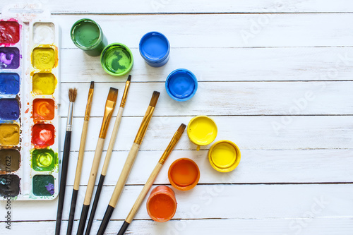 Paints and brushes on a white wooden background